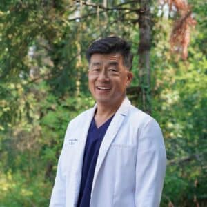 Dr. Lee in whitecoat and scrubs with forest background