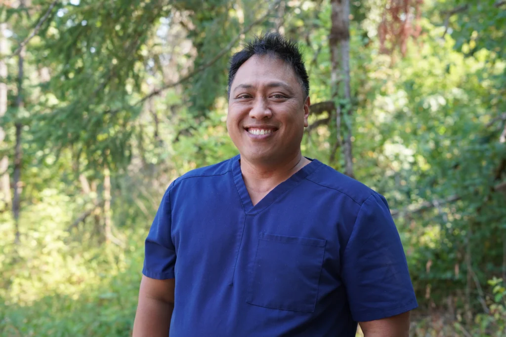 Dr. Ioane Ofisa, in blue scrubs with a nature background