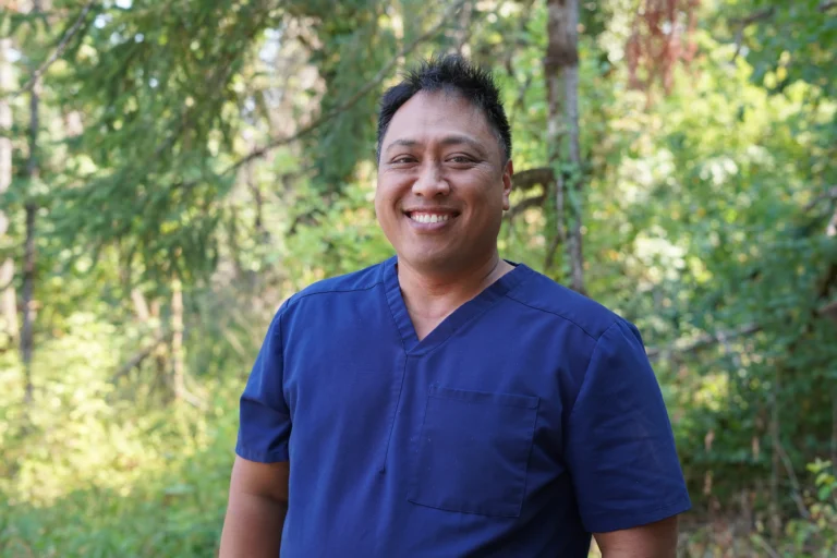 Dr. Ioane Ofisa, in blue scrubs with a nature background